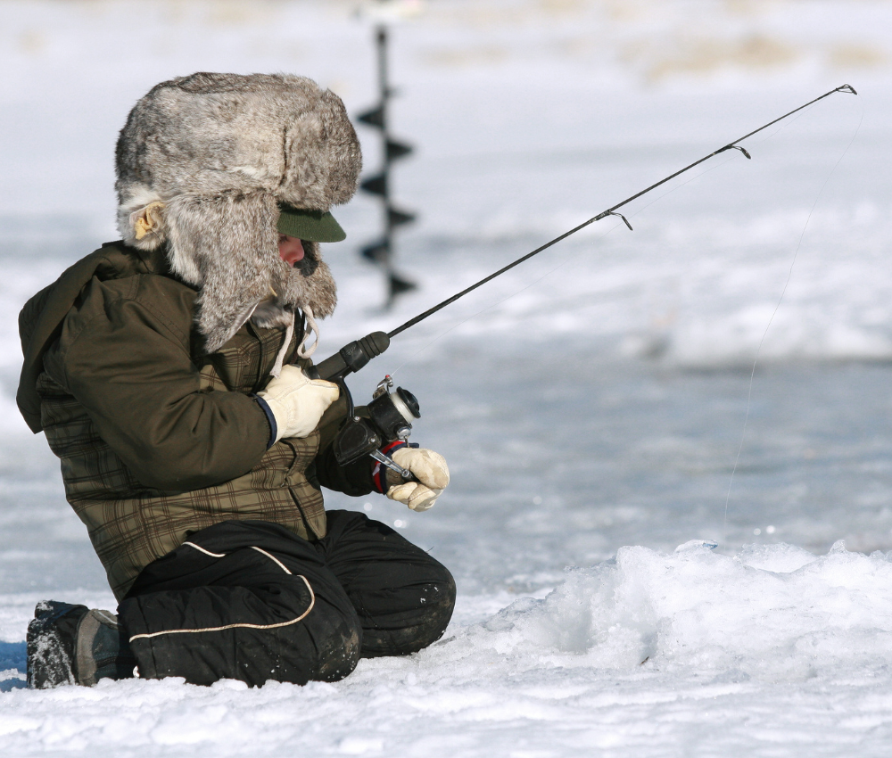 a small child with a fur hat holds a fishing rod on a frozen lake