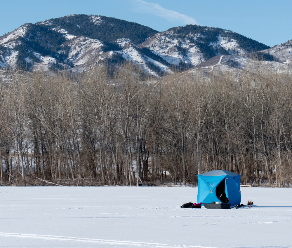 a blue tent on a frozen lake with a mountain in the background