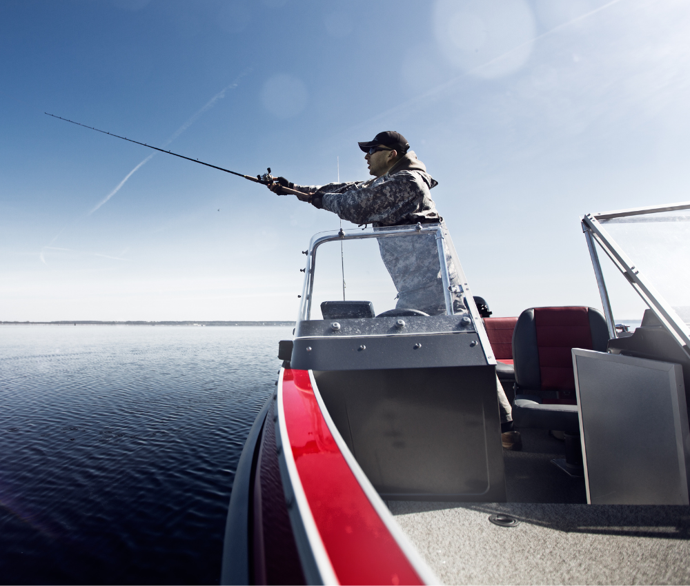man casts a fishing rod from a red boat