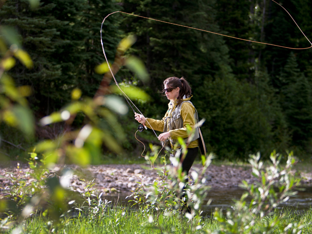 women stands in a river while fly fishing for trout